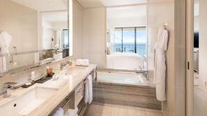 Un bagno moderno con uno specchio grande, due lavabi, una vasca da bagno e vista sul mare.