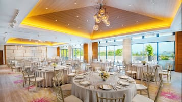 A spacious banquet hall with round tables set for dining, large windows offering views, and a modern ceiling design.