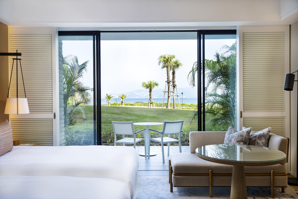 A hotel room with a large sliding glass door leading to a balcony with a view of a golf course and palm trees.