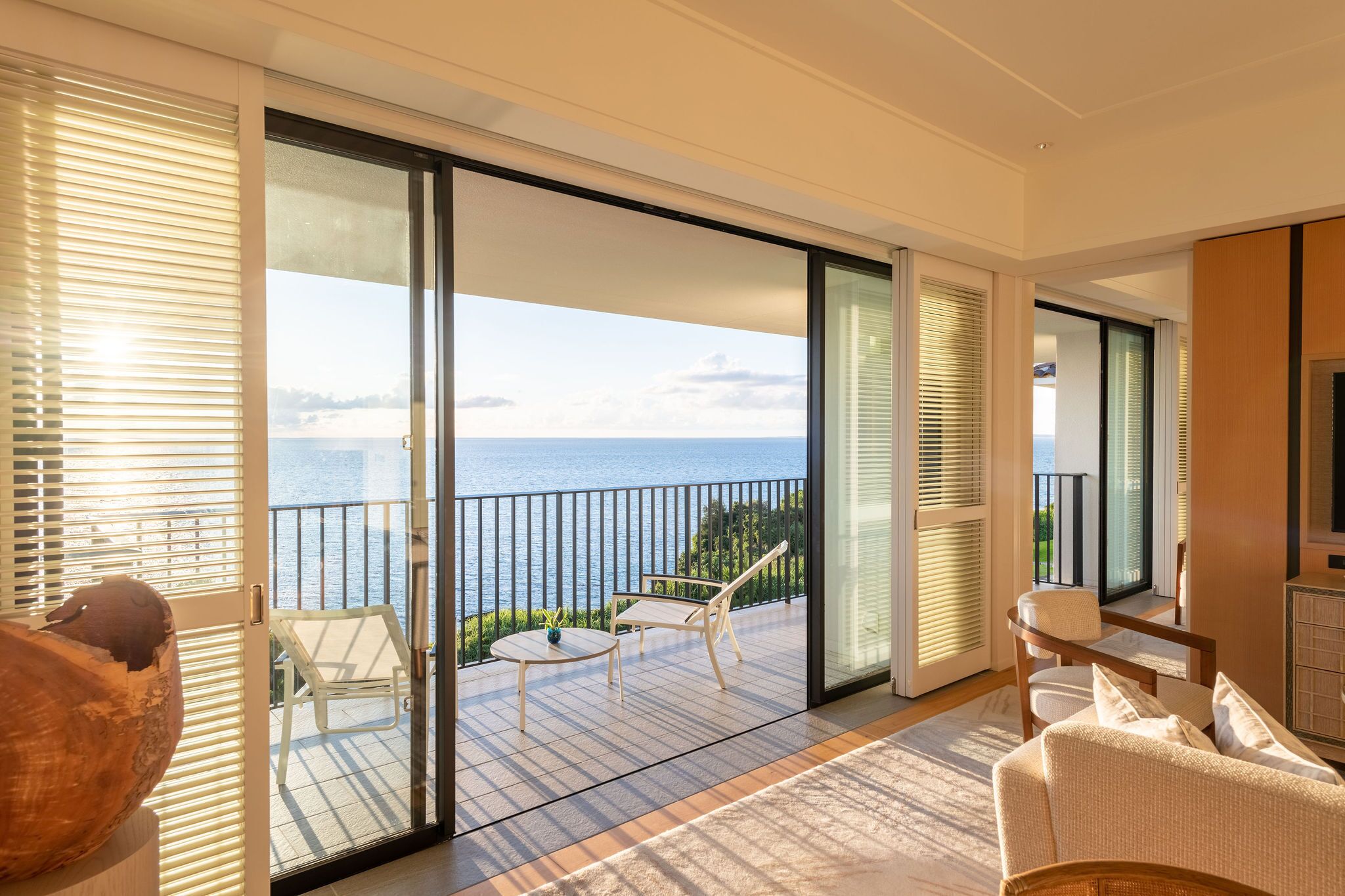 Un balcón con vista al mar, amueblado con una mesa y sillas, y una escultura de madera.