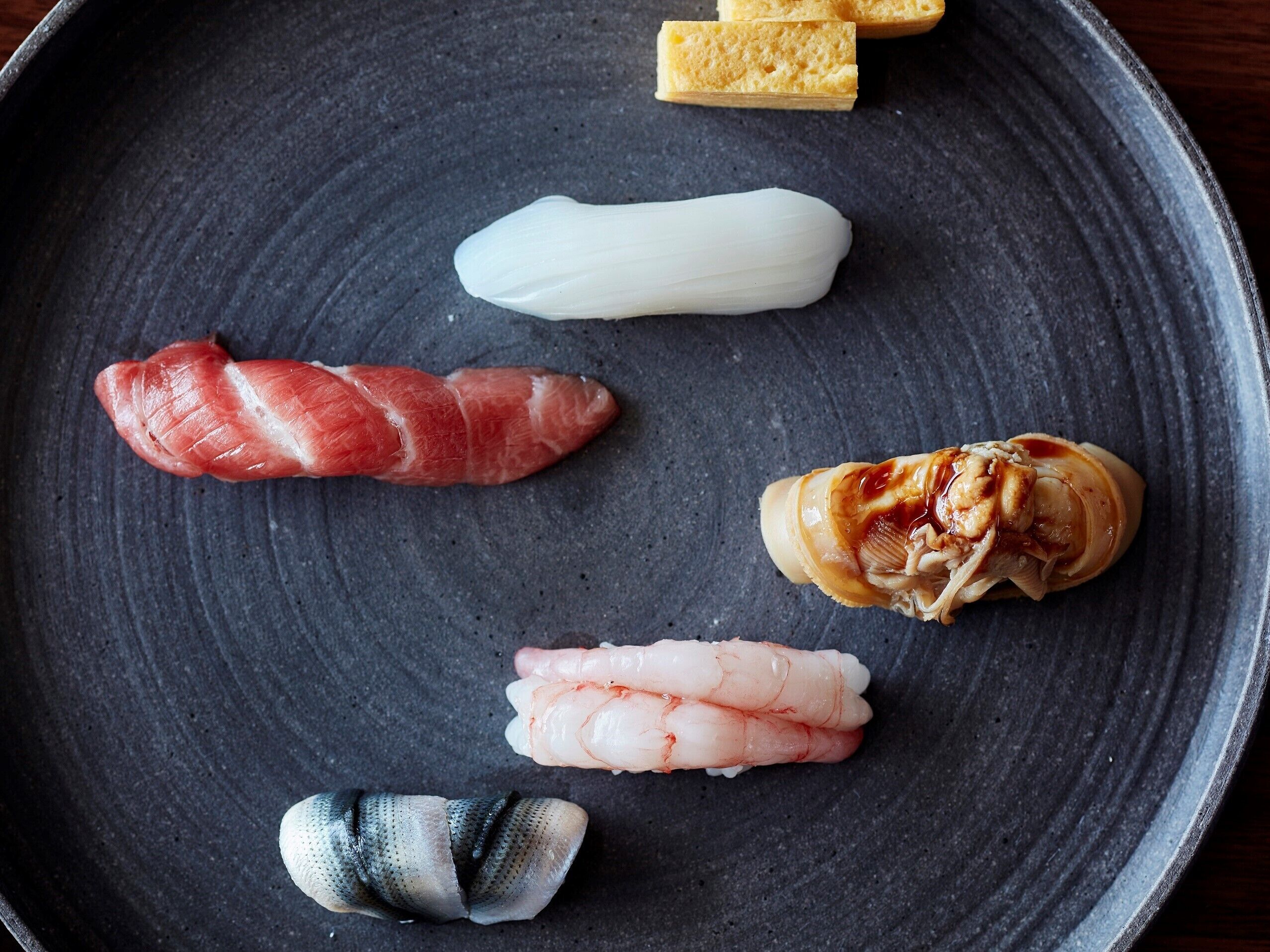 Een zwarte keramieken schaal met verschillende soorten sushi.