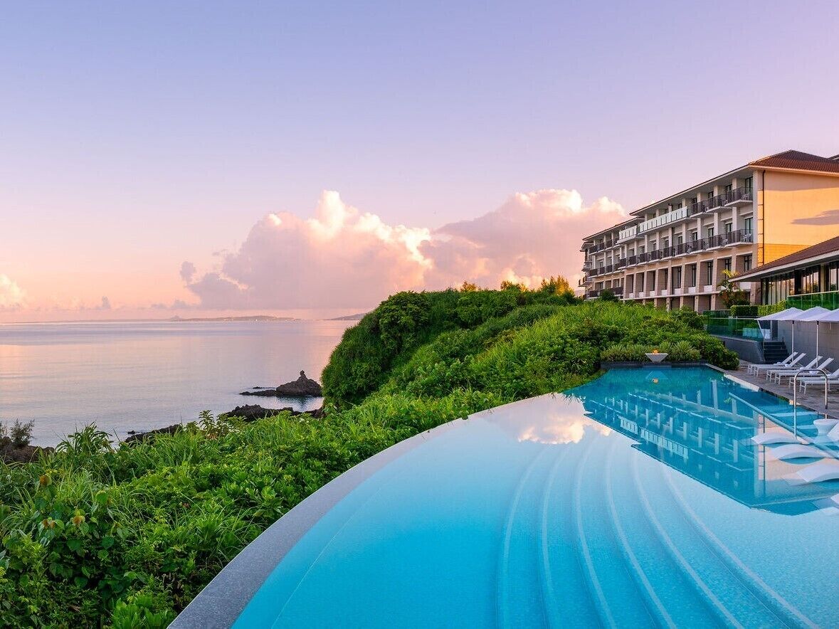 A resort pool with a clear view of the ocean and a hotel building in the background.