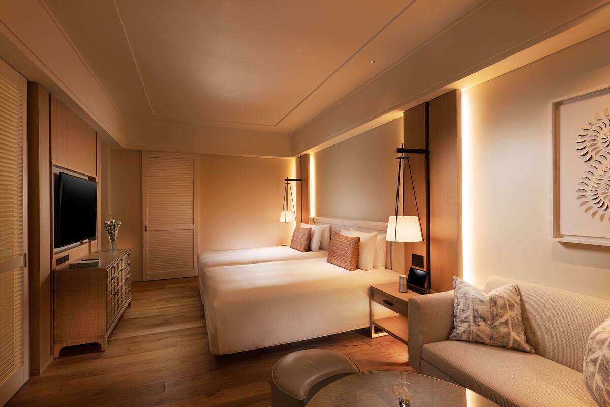 A hotel room with two beds, a TV, a desk, a sofa, and a small table.