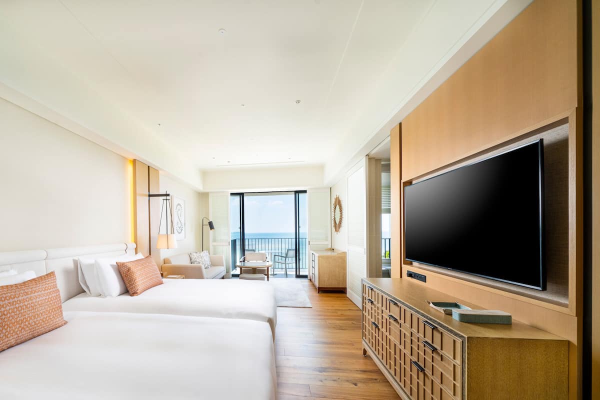 A hotel room with two large beds, a TV, a balcony with a view, and a wooden cabinet.