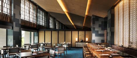 Un espace de restauration moderne dans un hôtel, avec de longues tables, des chaises et un tapis à motifs bleus.