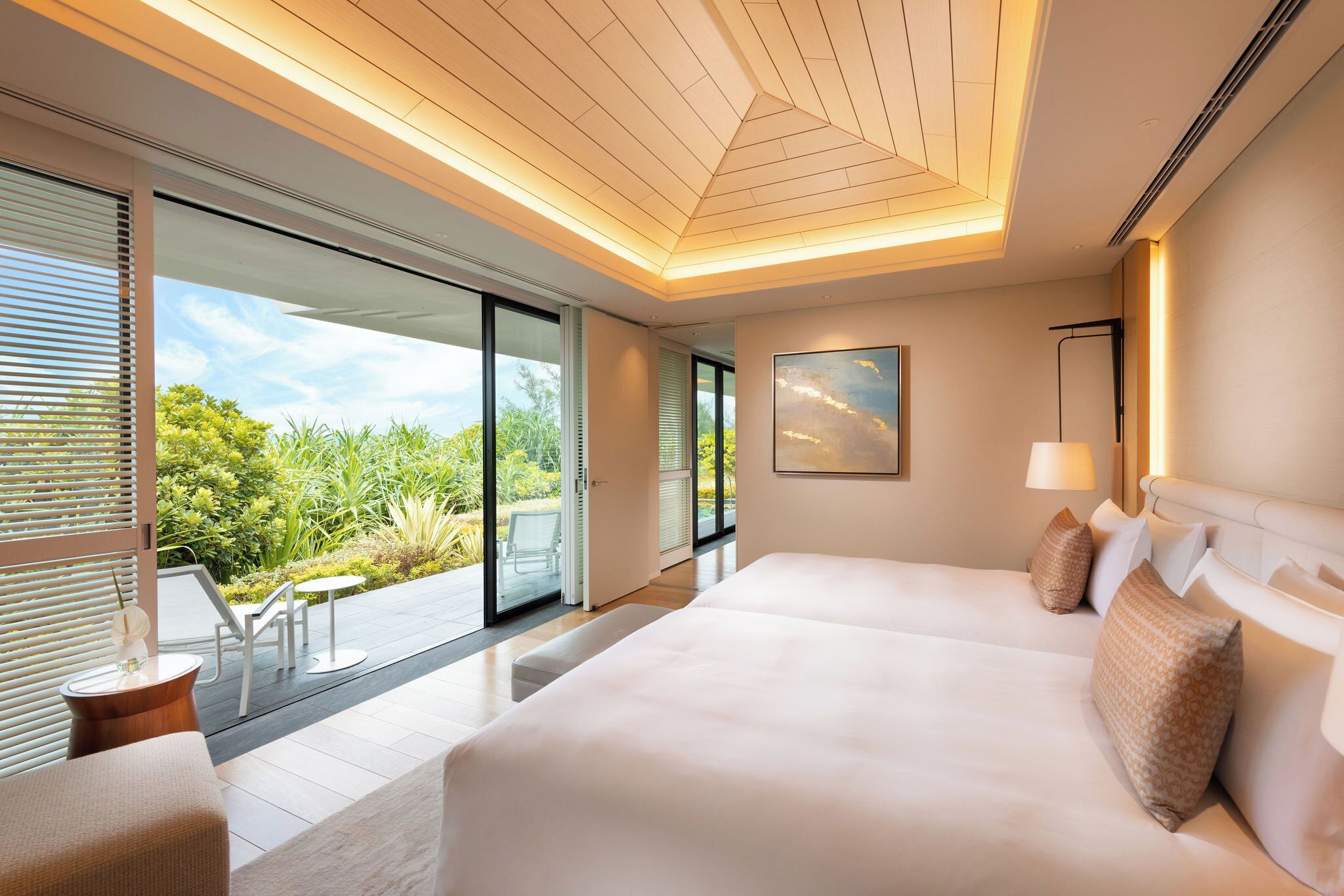A modern hotel room with a large bed, a balcony with a view of greenery, and a ceiling with a geometric design.
