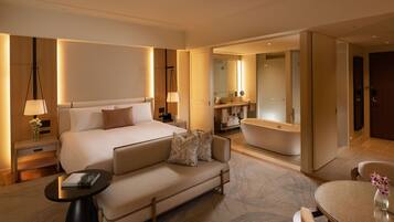 Ein modernes Hotelzimmer mit einem großen Bett, einer Couch, einem runden Tisch, einem Nachttisch, einer Lampe, einem Spiegel und einem Badezimmer mit einer Badewanne sowie einem großen Spiegel.