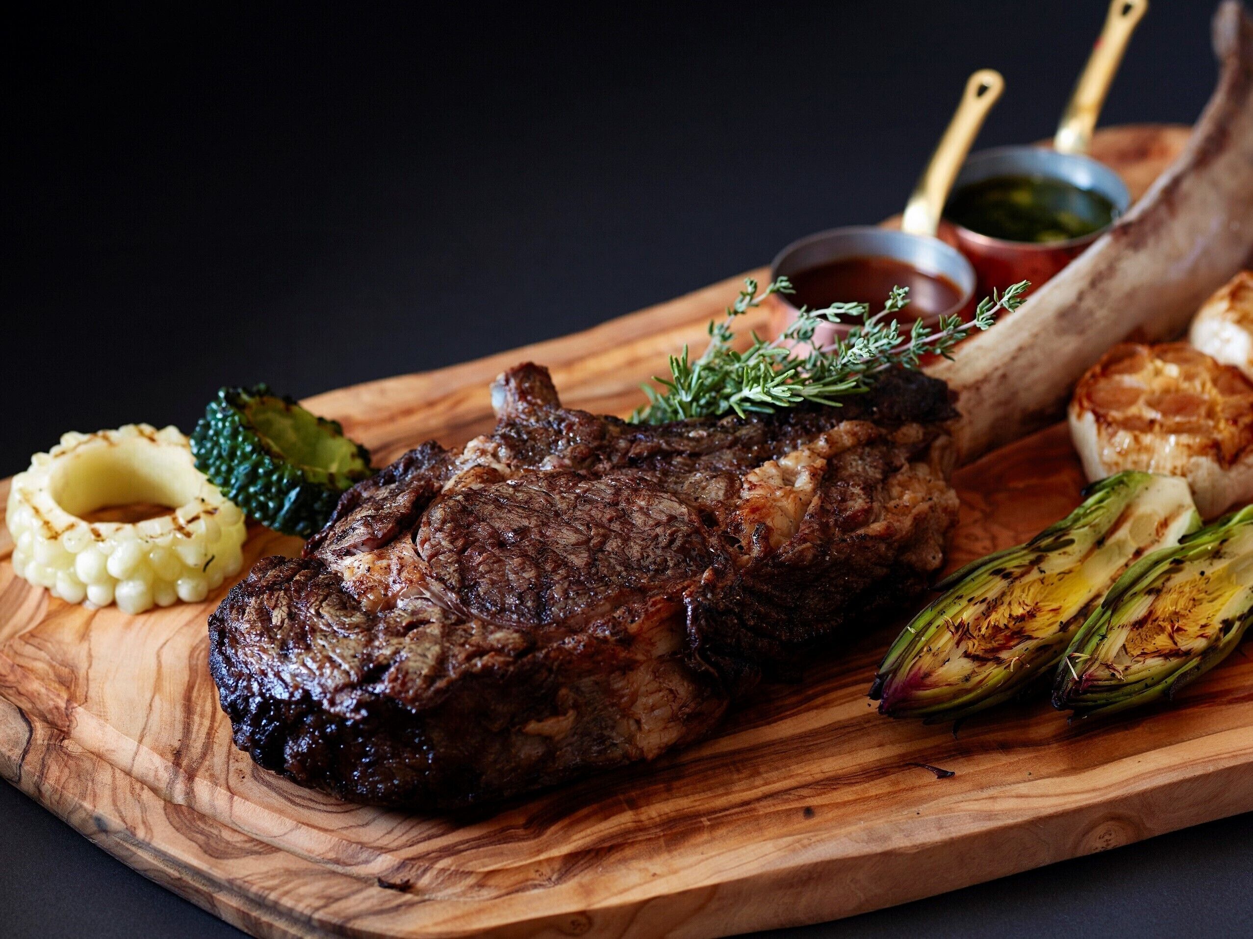 A steak with vegetables and sauces on a wooden board.
