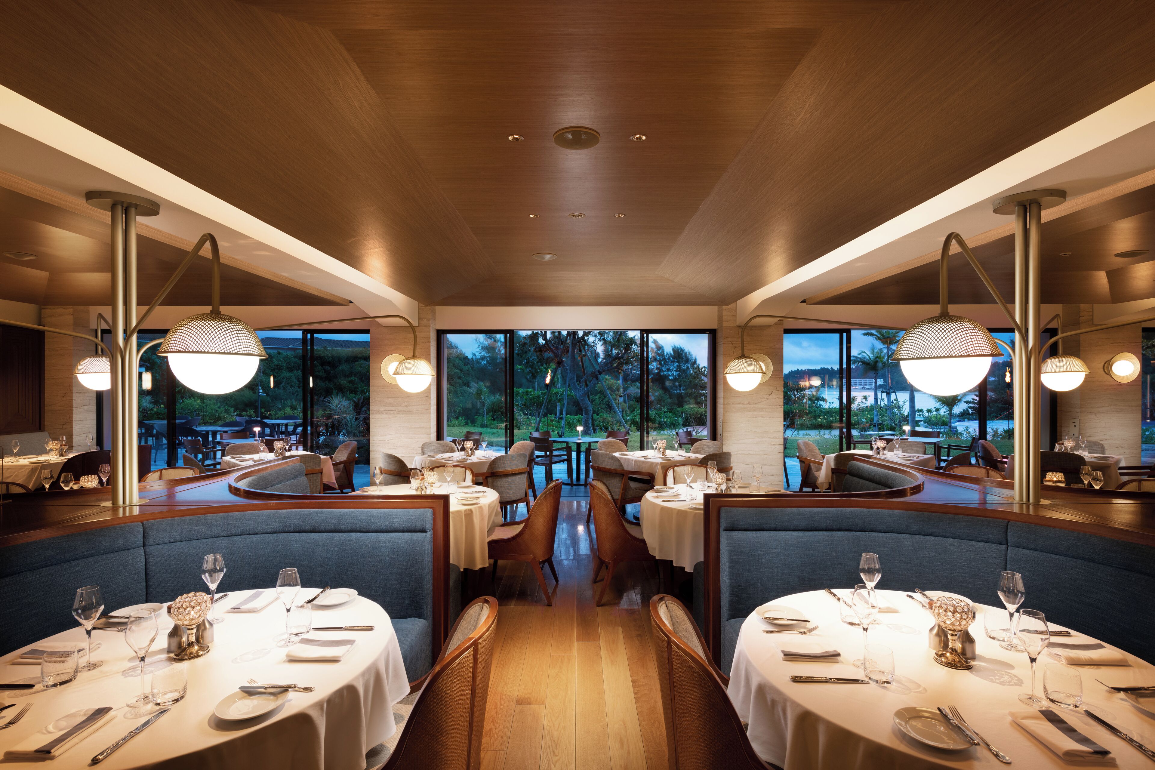 A restaurant with round tables, blue booths, and large windows offering a view of the outdoors.