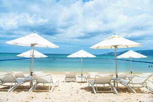 Una playa con sombrillas blancas y sillas de descanso.