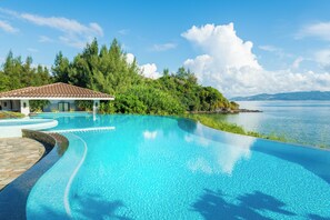 A swimming pool with a curved edge, surrounded by lush greenery and a view of the sea. - Halekulani Okinawa (Onna)