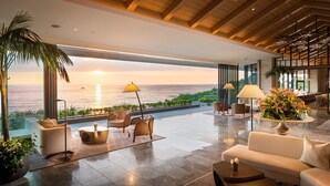 Un'ampia hall con vista sull'oceano al tramonto, arredi moderni e un soffitto alto con travi in legno.