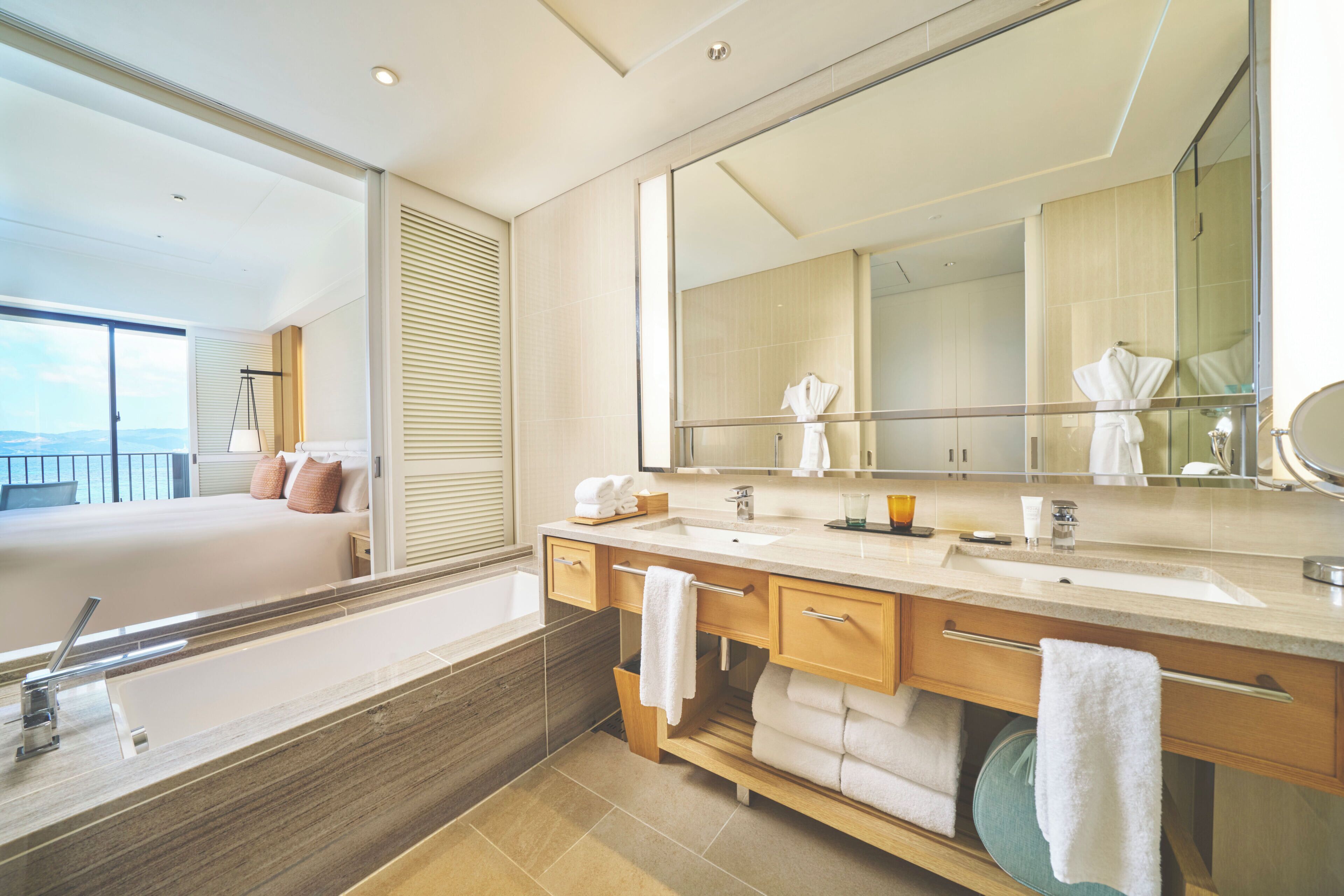 A modern bathroom with a large mirror, two sinks, and a bathtub.