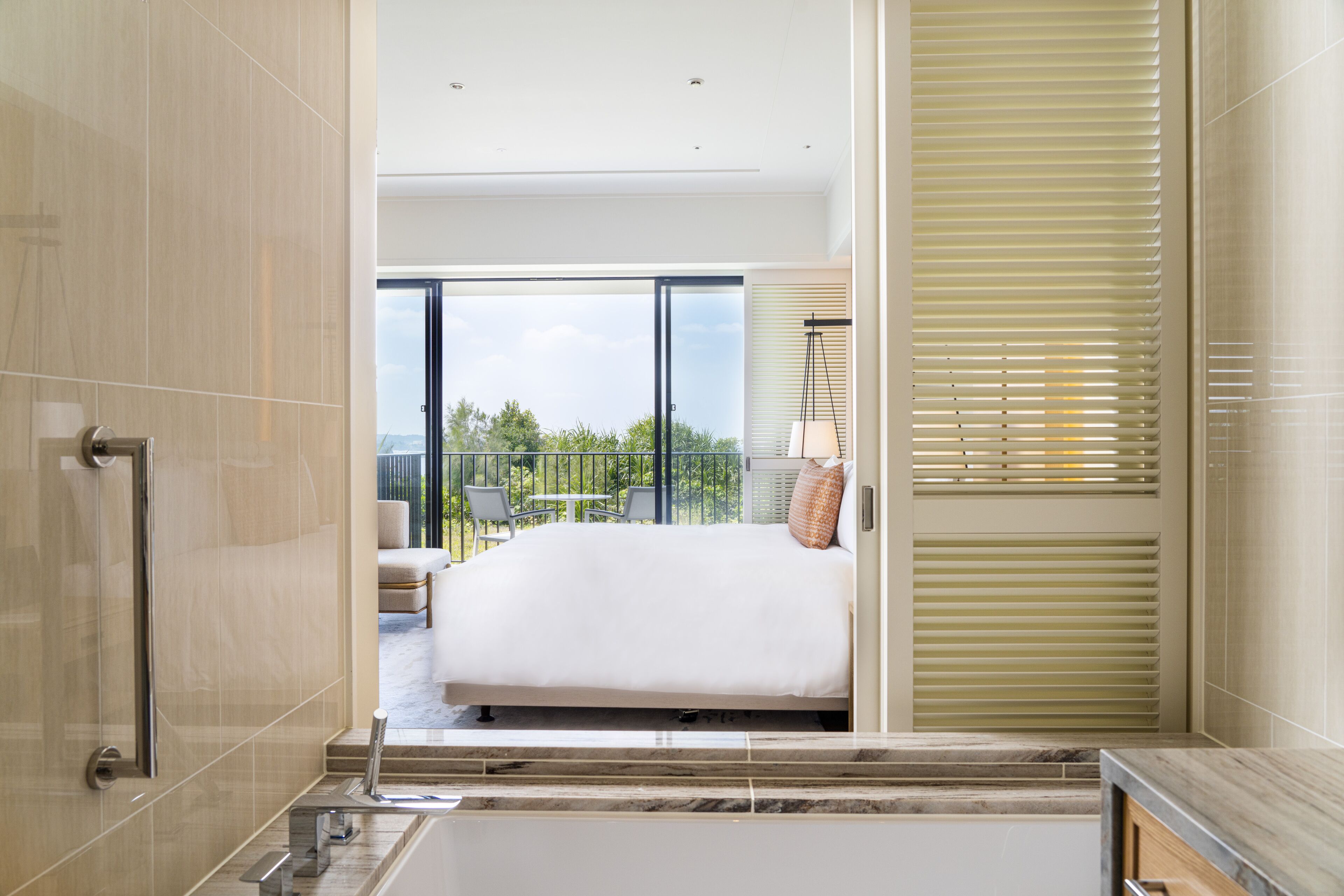 Quarto de hotel moderno com uma cama grande, uma varanda com área de estar externa e vista para a paisagem urbana.