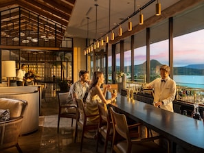 A modern bar area with a long counter, seating, and a view of a body of water.