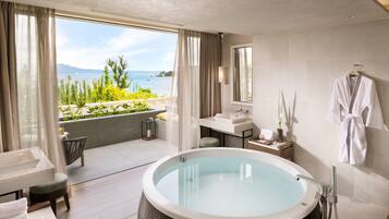 A modern bathroom with a large bathtub, a sink, and a mirror. There is a view of the sea through large windows.