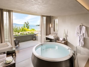 A modern bathroom with a large bathtub, a sink, and a mirror. There is a view of the sea through large windows.