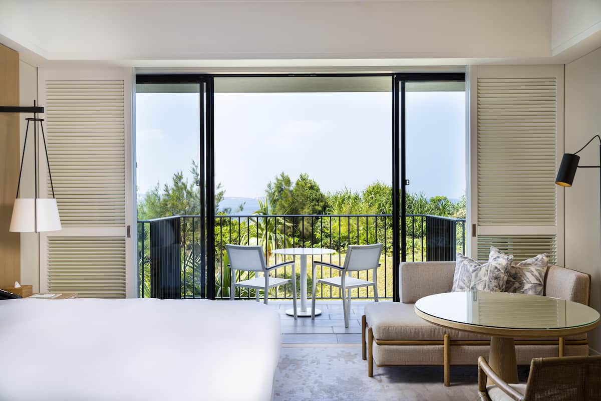 A hotel room with a balcony, a bed, a round table, and two chairs.