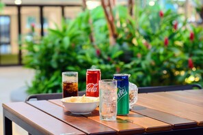 A wooden table with a bowl of chips, two glasses of soda, and two cans of soda. - Savv Hotel (George Town)