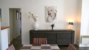Een moderne woonkamer met een eethoek, met een donkerbank, een gestreepte fauteuil en een tafel met een geruit tafelkleed.