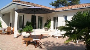 Een overdekt terras met tuinmeubilair, een tafel en een grote parasol.