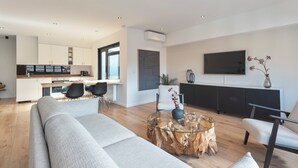 Un salon moderne avec un canapé, une table basse en verre et un coin repas comprenant des chaises, et une cuisine en arrière-plan.
