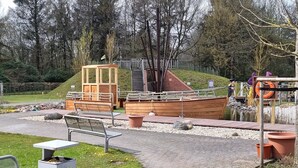 Eine hölzerne Bootsanlagemit Bänken, einem Mülleimer und einem Rettungsring in Wassennähe.