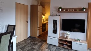 Ein modernes Wohnzimmer mit Flachbildfernseher an einer Holzablage, einem eingebauten Backofen und einer Küche im Hintergrund.