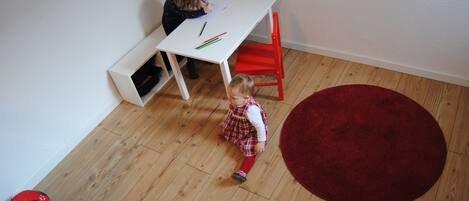 A child sitting at a white desk with a red chair, a red rug, and wooden flooring.