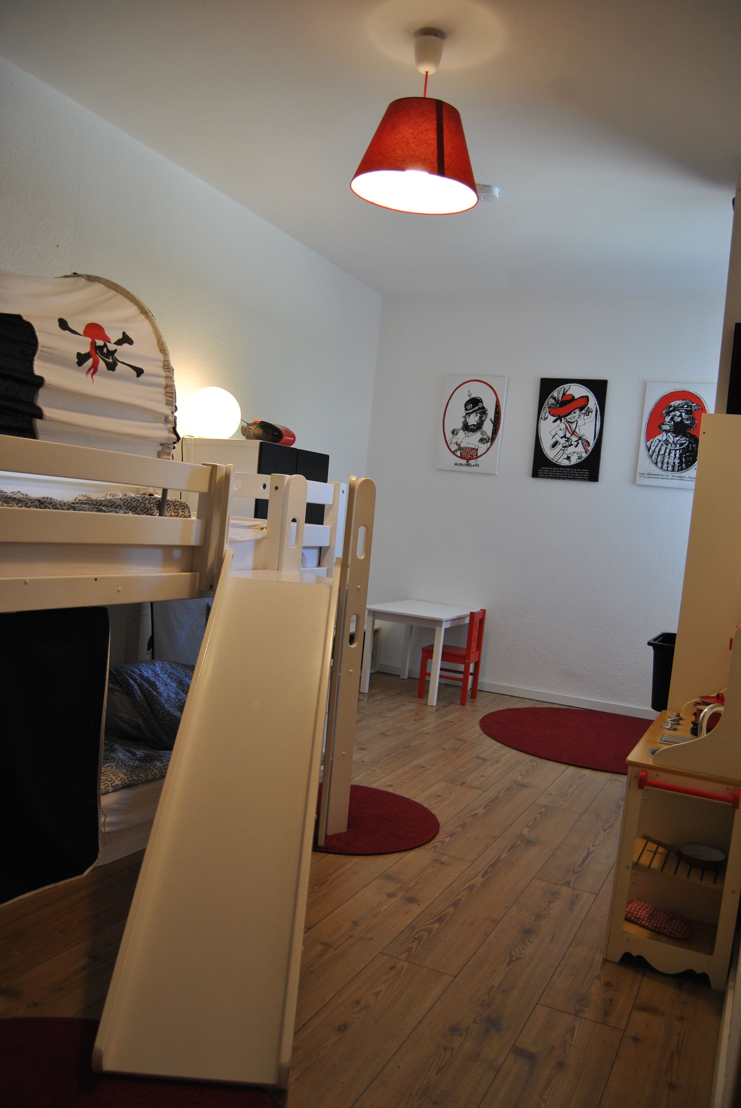 A room with bunk beds, a desk, a chair, and a red lamp.