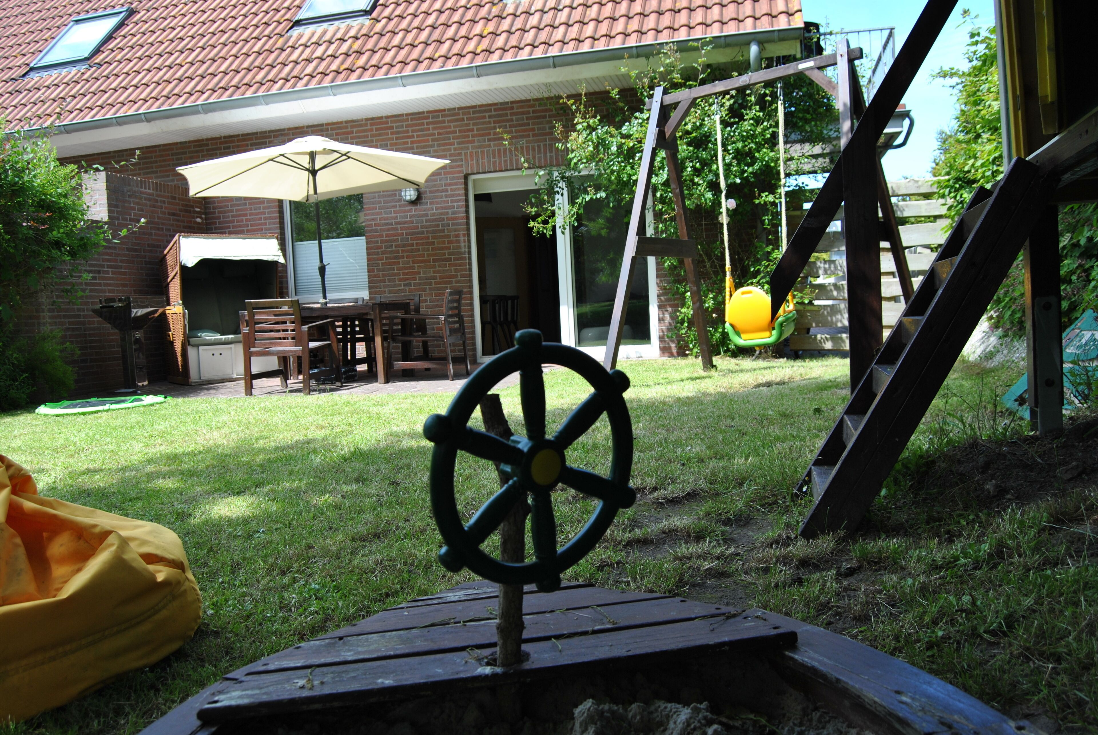 Un patio trasero con una casa de ladrillo, un columpio, una terraza de madera y una bolsa amarilla.