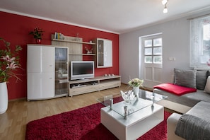 A modern living room with a red accent wall, a white entertainment unit, a glass coffee table, and a grey sofa.