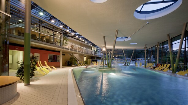 Piscina interior con vista despejada al área de la piscina, tragaluz y zona de estar con sillas amarillas.