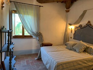 Une chambre à coucher comprenant un lit, une table de chevet, une fenêtre avec des rideaux et un luminaire fixé au mur.