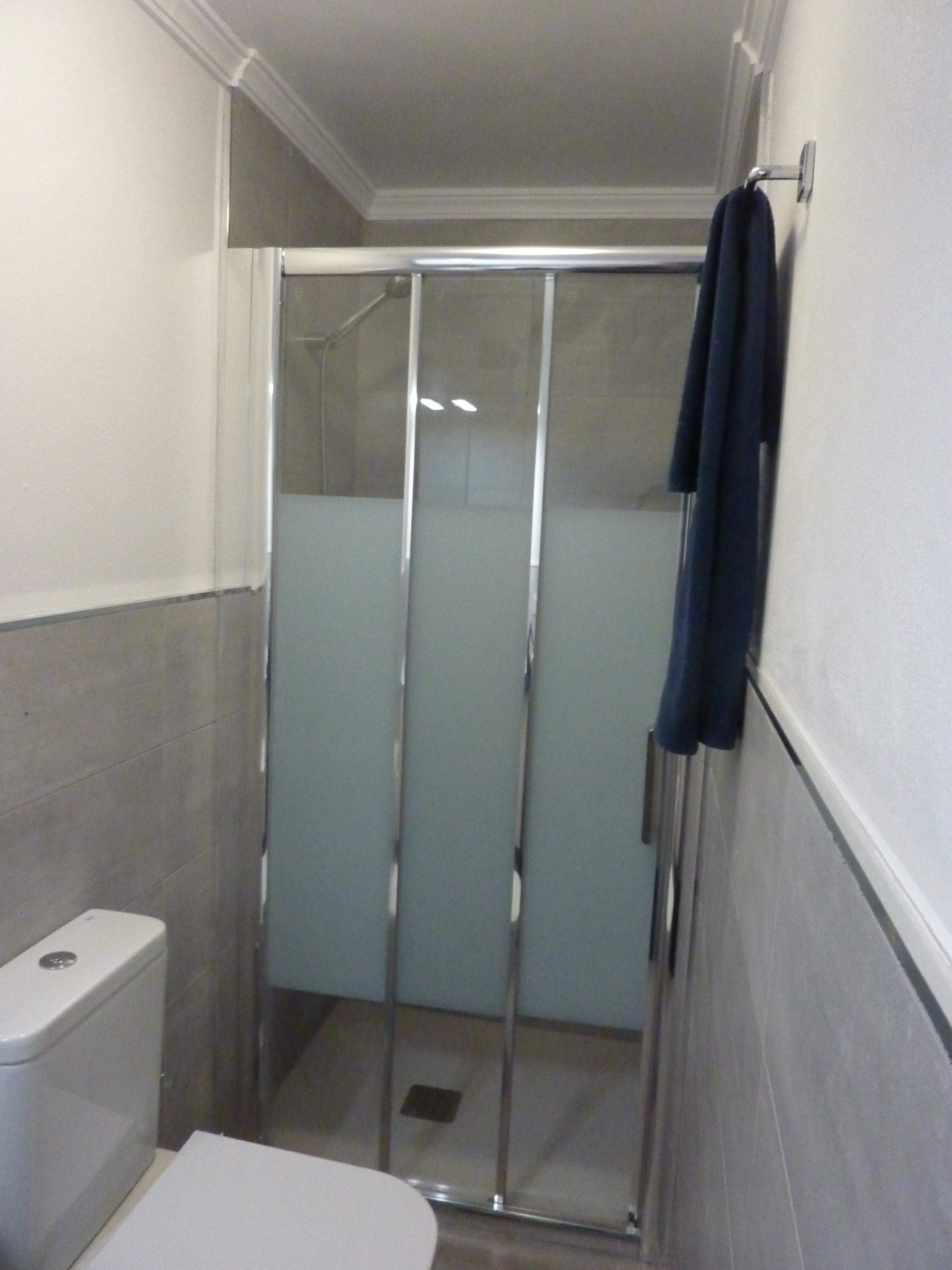 A small bathroom with a toilet, a glass shower enclosure, and a towel hanging on the wall.