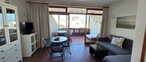 A room with a dining area, a sofa, a TV, and a view to the outside.