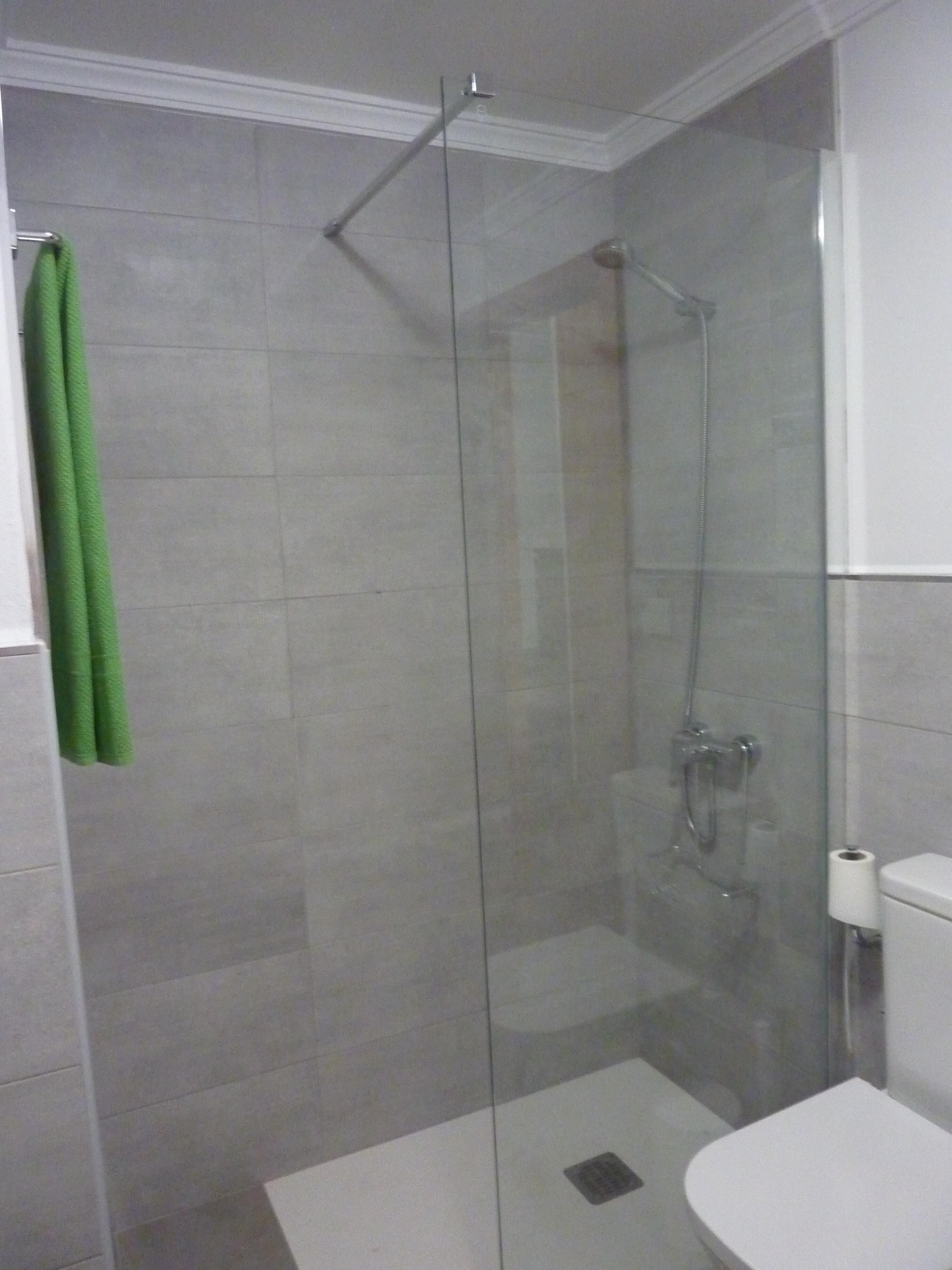 Une cabine de douche fermée par des parois en verre, avec des toilettes blanches et une serviette verte suspendue à un porte-serviettes.