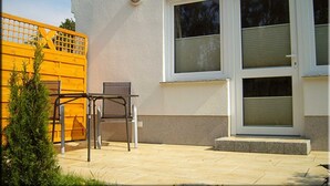 A patio with a table and chairs, a yellow fence, and a building with a white exterior and large windows.