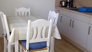 A dining area with a white table and chairs, a hanging light fixture, and a microwave above a wooden countertop.