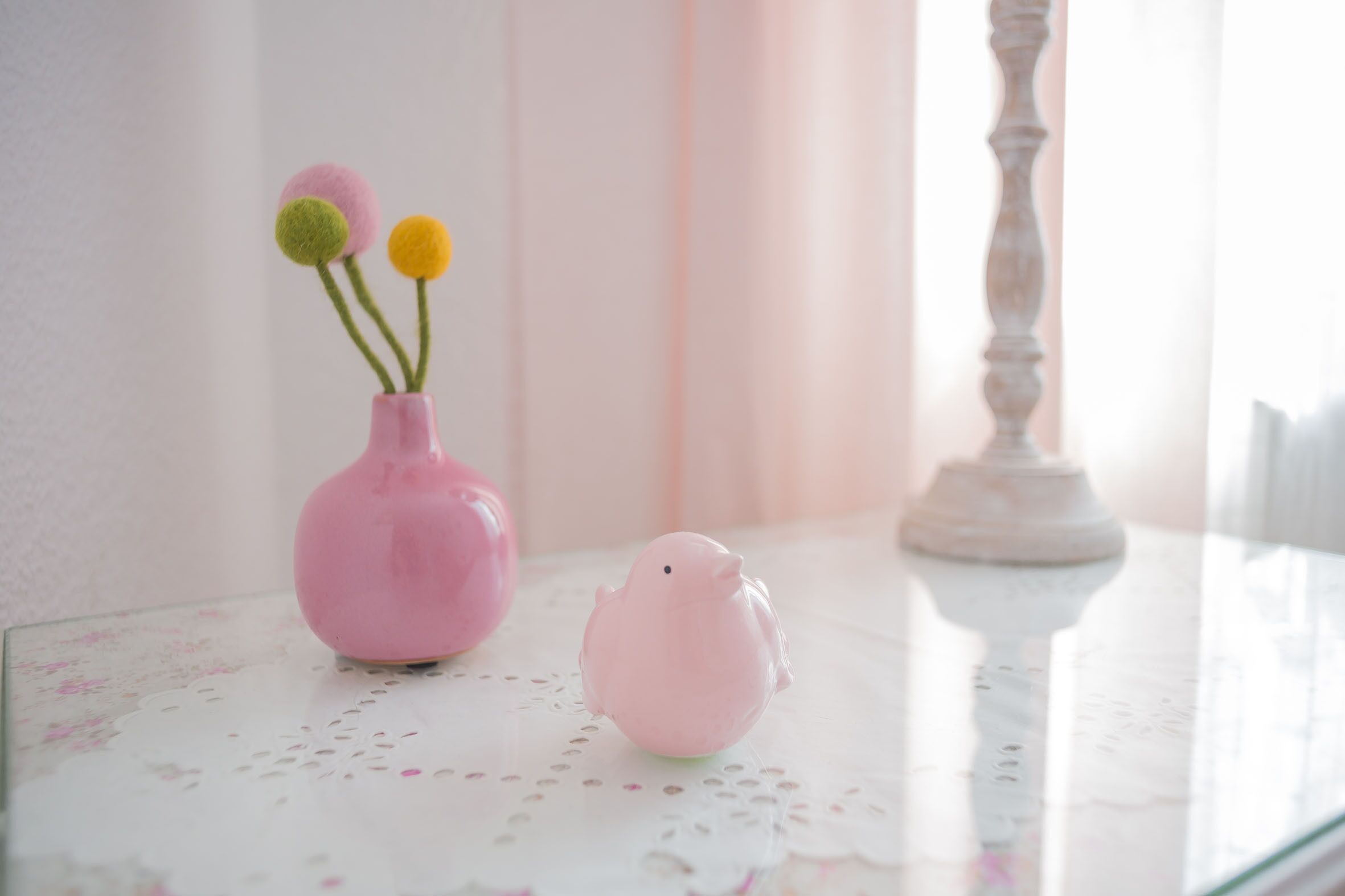 A pink vase with three felt flowers on a lace tablecloth.