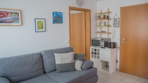 Un salón con un sofá gris, un microondas y un armario blanco pequeño. Hay dos puertas, una abierta y otra cerrada.