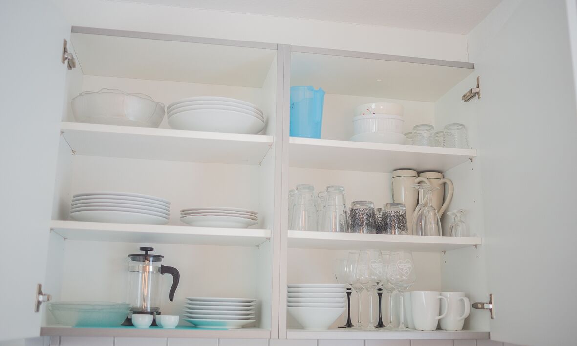 Una cocina con gabinetes blancos, estantes con vajilla, vasos y una cafetera.