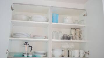Una cocina con gabinetes blancos, estantes con vajilla, vasos y una cafetera.
