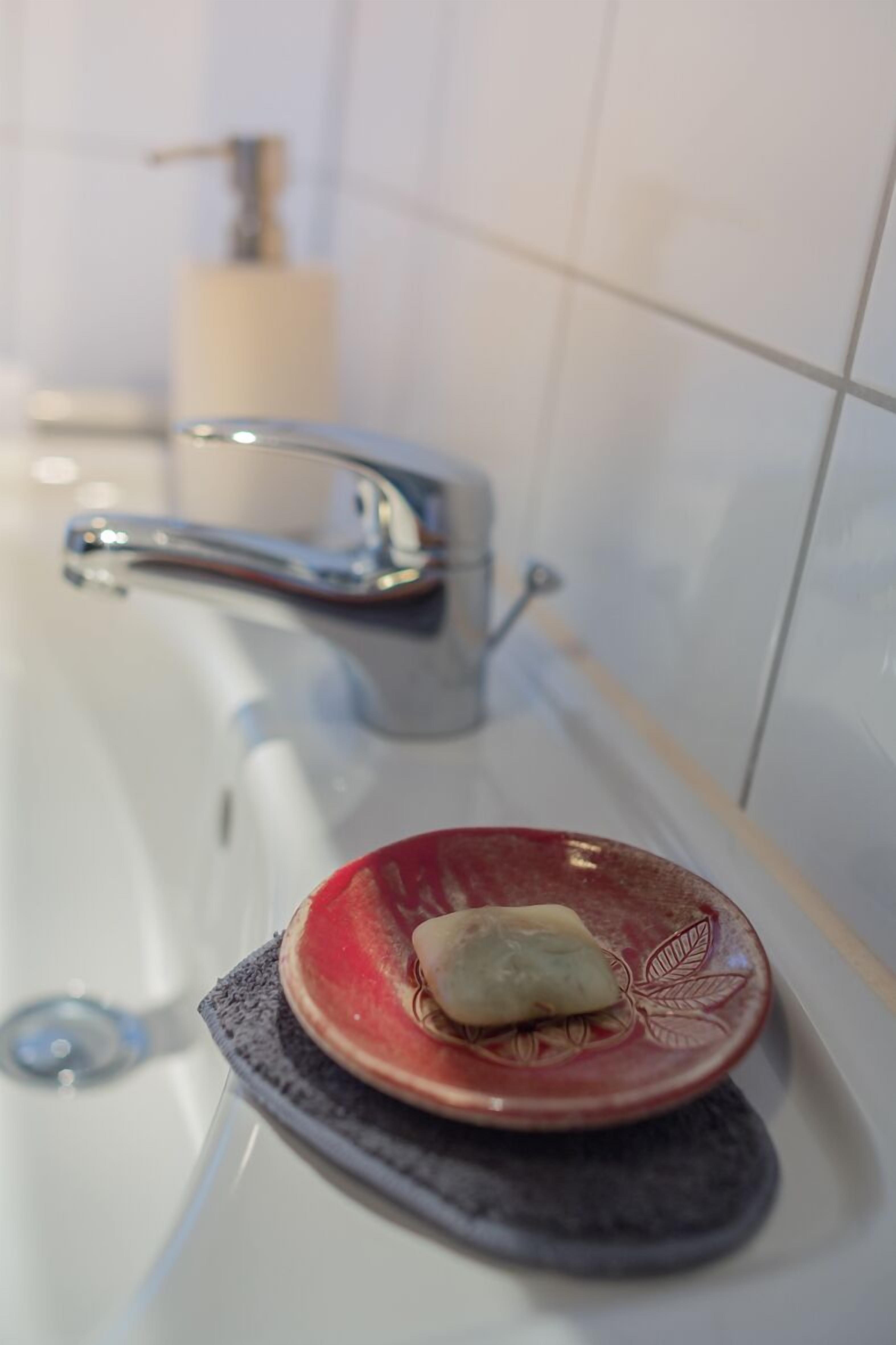 A bathroom with a white sink, a red soap dish, and a soap bar.