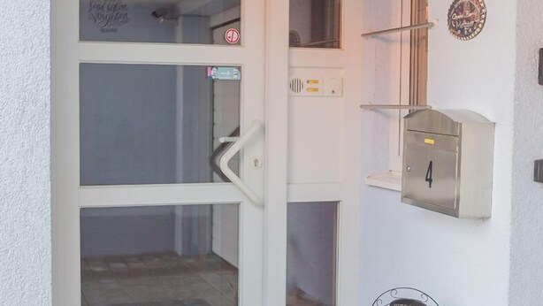 Una puerta blanca con panel de vidrio, un buzón, un letrero de bienvenida y una pequeña cesta con plantas.