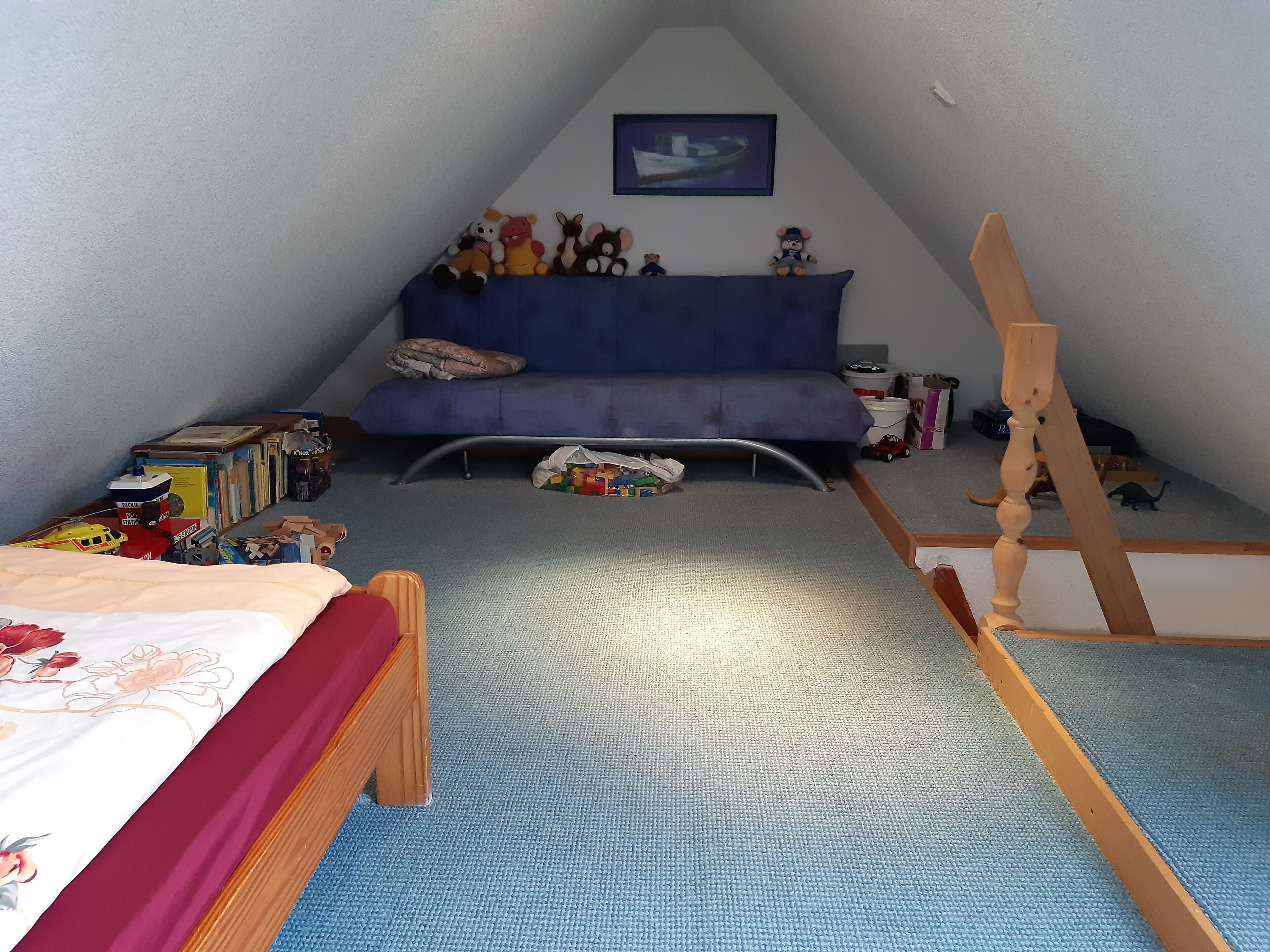 Une petite pièce aux murs inclinés, avec un canapé bleu, un lit recouvert d’une courtepointe à motifs floraux et une échelle en bois.