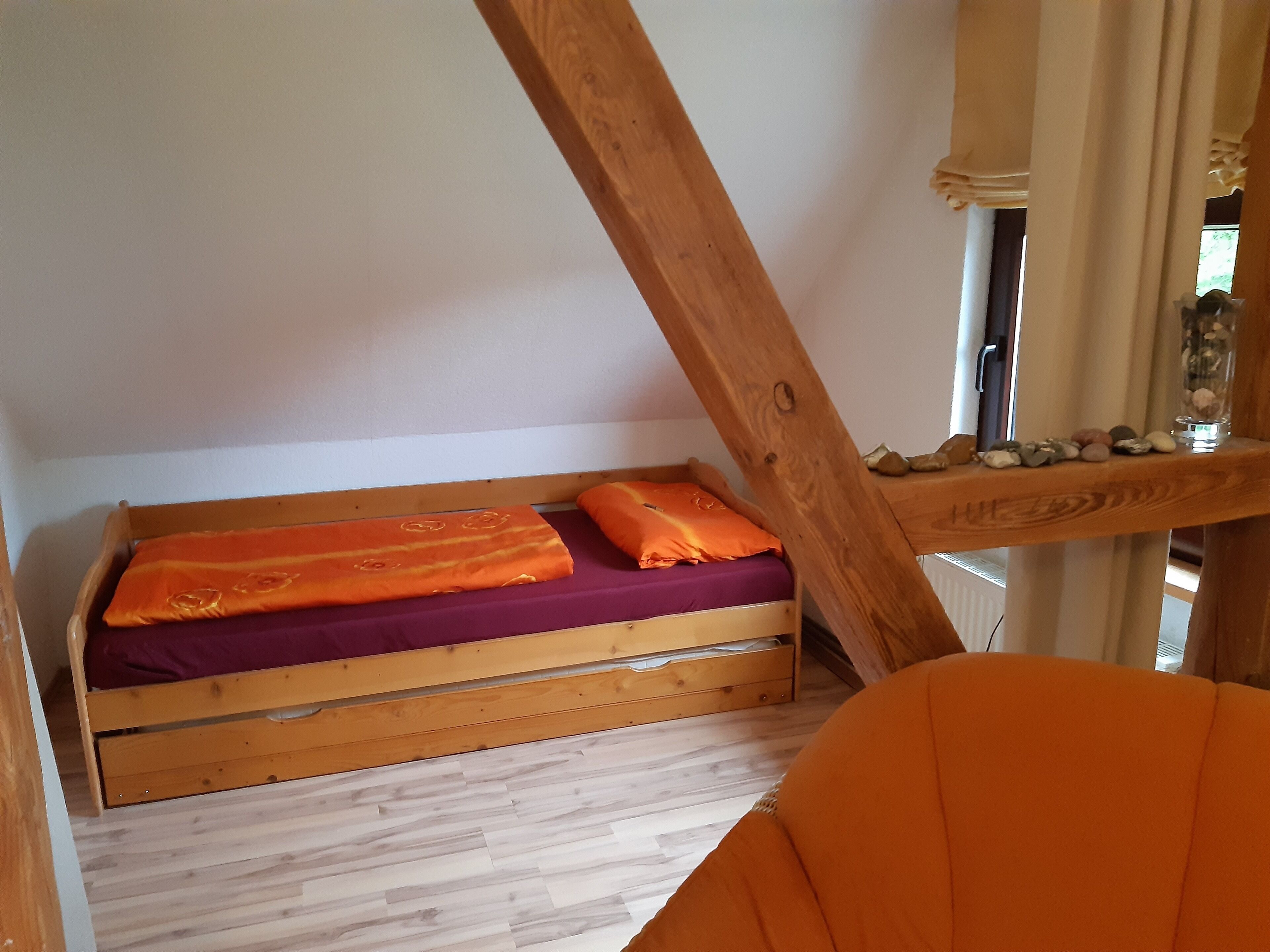 Tyylikkäässä, avoimessa makuuhuoneessa on puinen sängynrunko, violetit ja oranssit vuodevaatteet sekä puinen pääty.