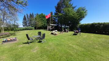 Enjoy a serene outdoor space with a picnic table, chairs, and a swing set amidst lush greenery and a natural backdrop.