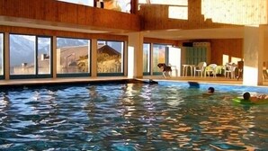 An indoor swimming pool with clear windows, a wooden interior, and a view of mountains. - Stylish loft with a great panoramic view (Veysonnaz)