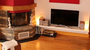 A modern living room with a stone fireplace, a flat-screen TV, and a red abstract painting on the wall. - Stylish loft with a great panoramic view (Veysonnaz)